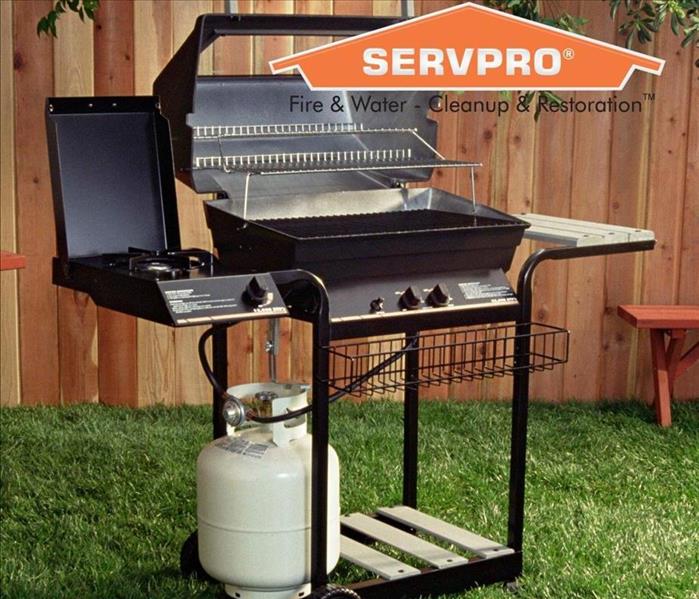 A propane grill sitting in a yard with the SERVPRO logo.
