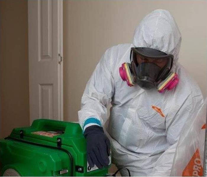 A SERVPRO technician in full personal protective equipment with a piece of SERVPRO equipment.