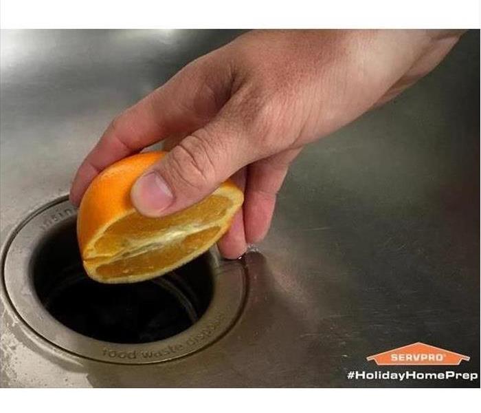 A hand squeezing an orange of a sink drain.