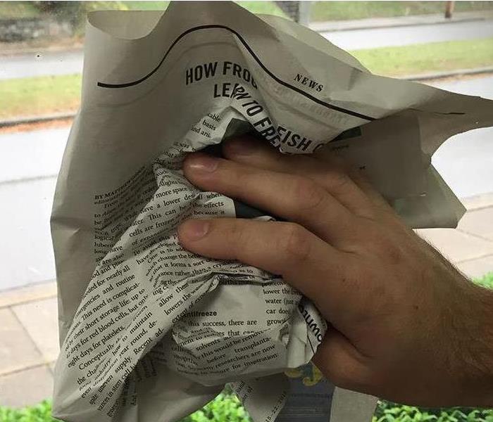 A hand using newspaper to clean windows.